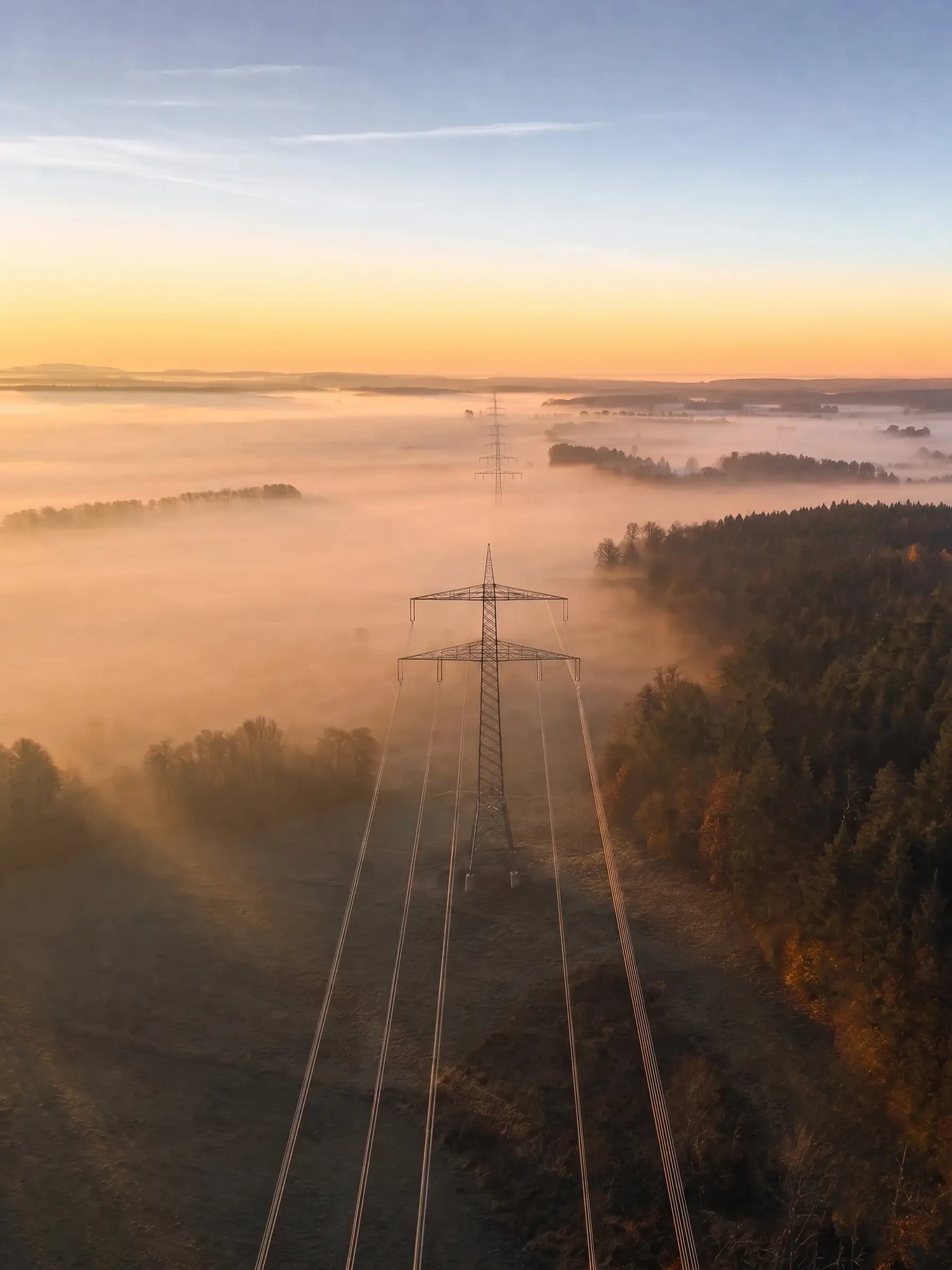 Blick von der Traverse eines Freileitungsmastes entlang der Leiterseile in die Trasse, Morgennebel